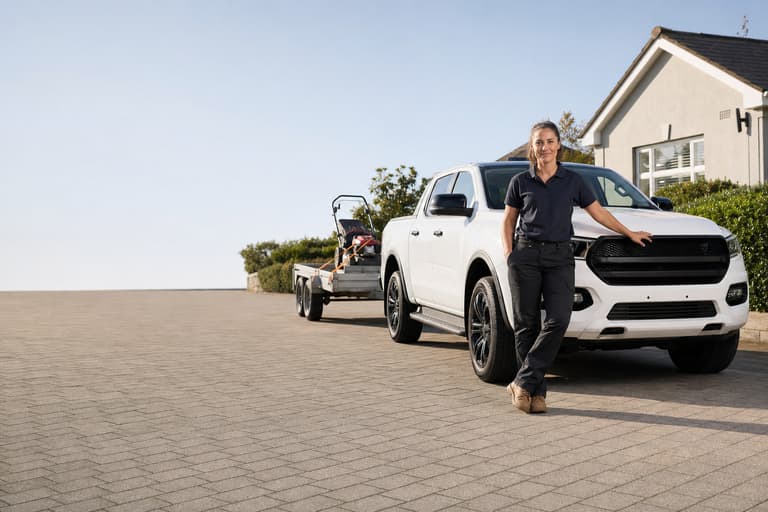 A lawn care business owner beside her truck and trailer on a suburban driveway
